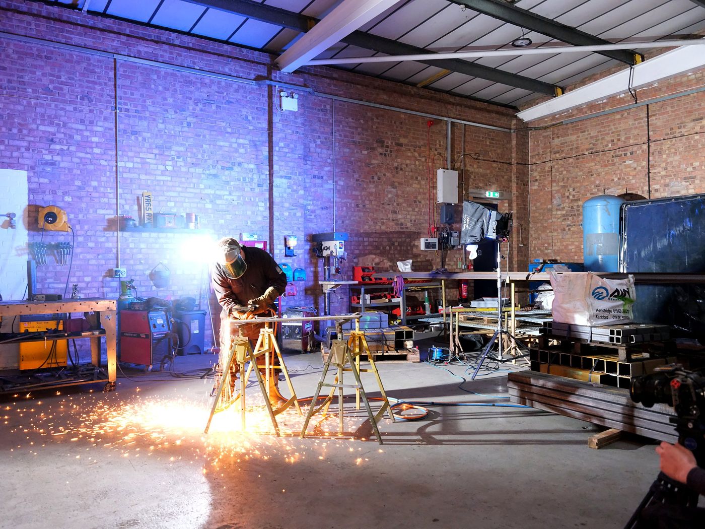 CCM filming a welder at work, sparks lighting the workshop